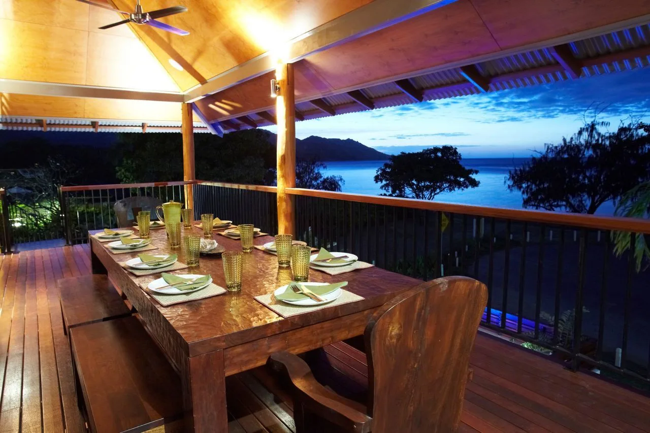 An outdoor dining area with a set table overlooks the water at dusk.