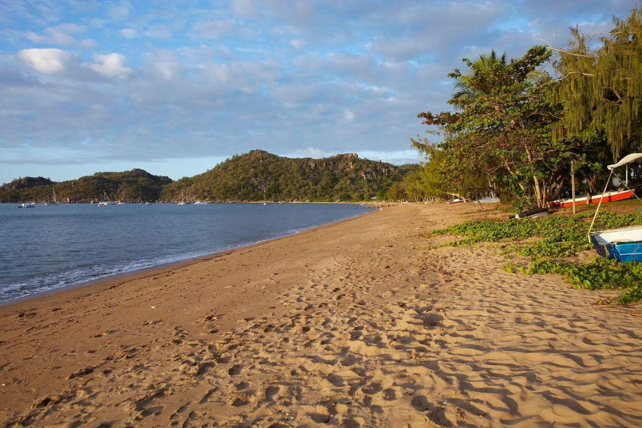 A sandy beach curves along calm water, with wooded hills across the bay.