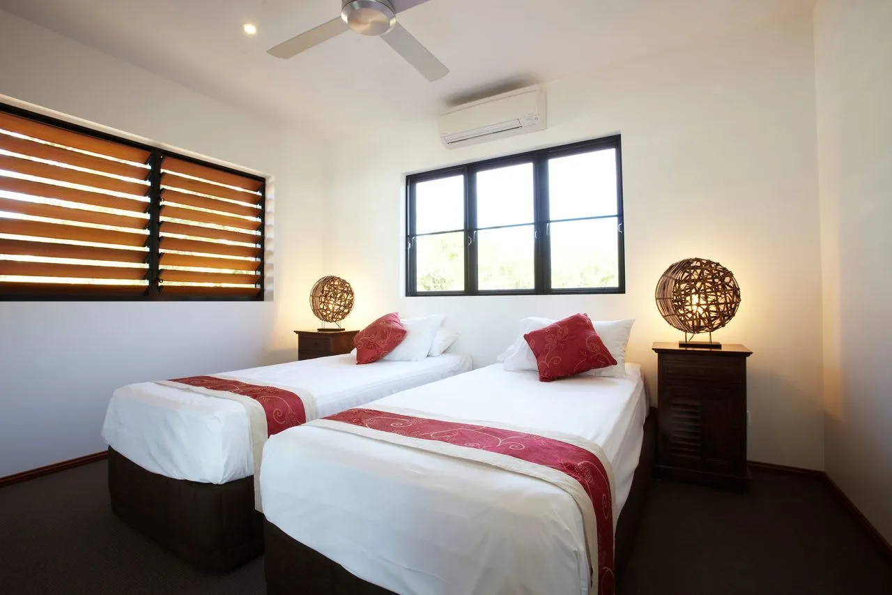 A bright bedroom with two beds and red accents.