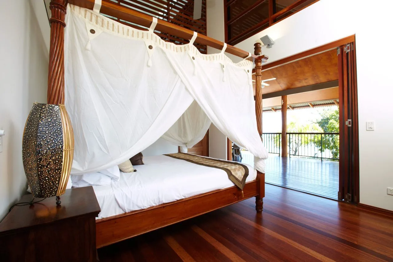 A bedroom with a wooden four-poster bed draped in white fabric.
