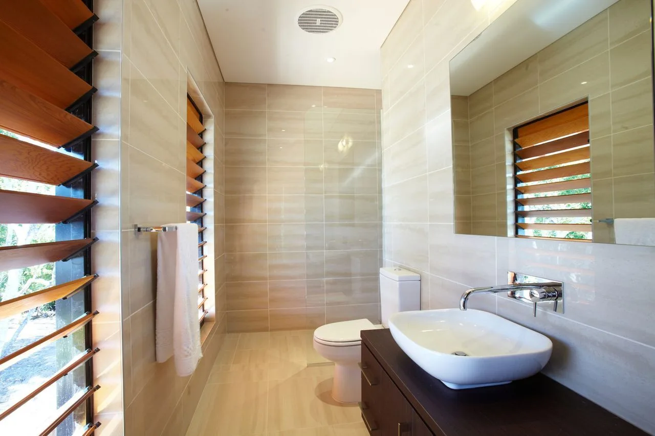 A tiled bathroom with a sink, toilet, and louvered windows.