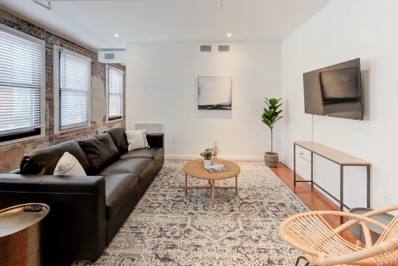 A bright living room with seating, a patterned rug, and a wall-mounted television.