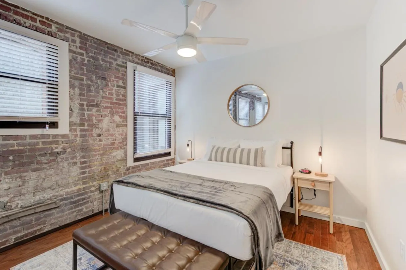 A bedroom with a bed, exposed brick wall, and two windows.
