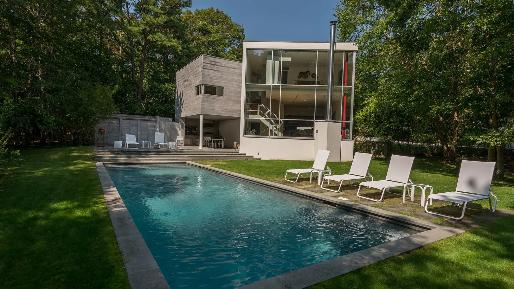 Una piscina está junto a una casa moderna con fachada de vidrio y césped.