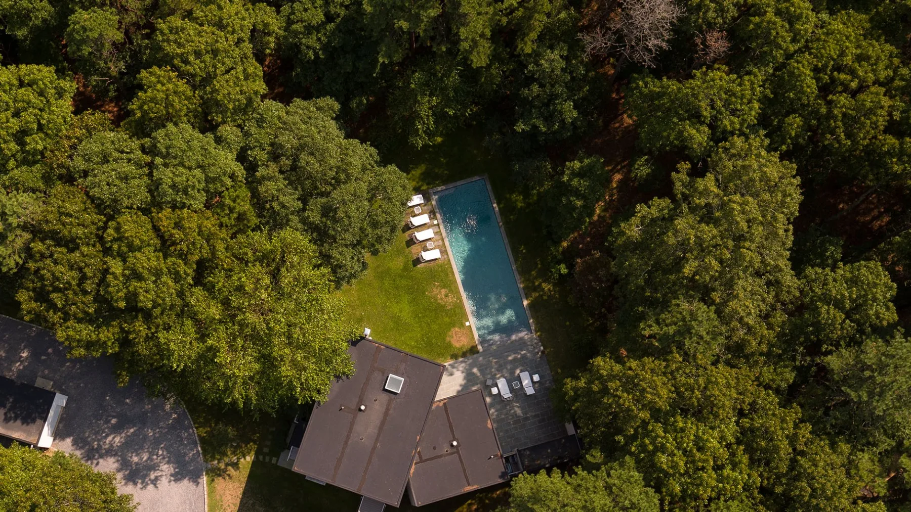 Aerial view of a swimming pool beside a building, surrounded by trees.