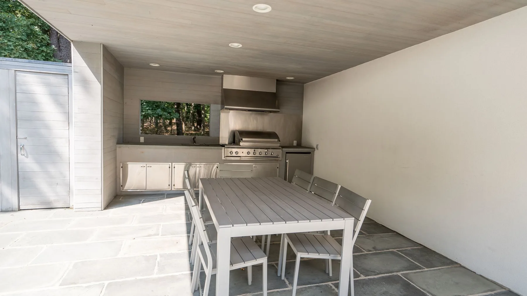 Un comedor en un patio cubierto con una mesa larga y una cocina exterior.