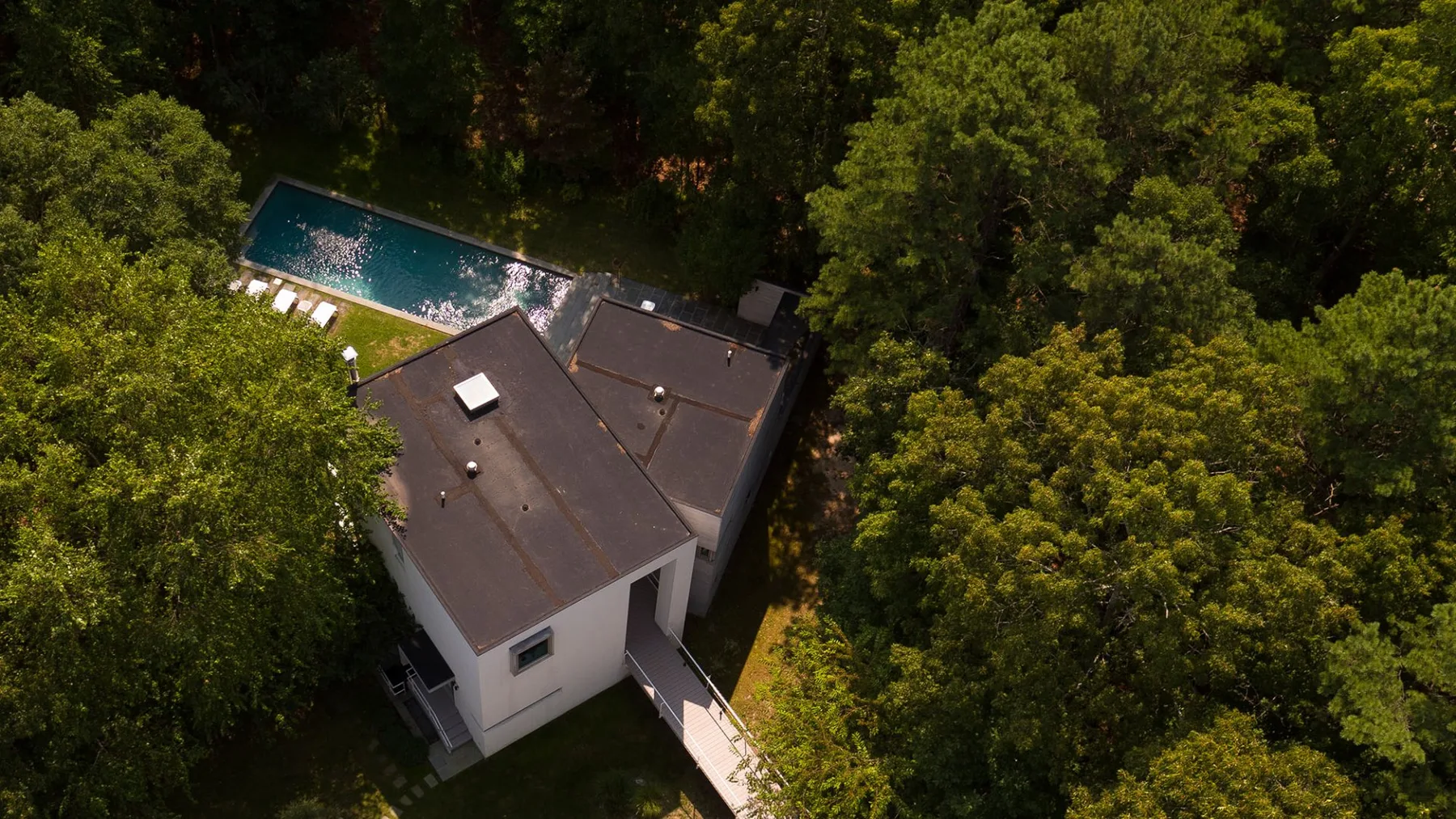 Aerial view of a house surrounded by trees, with a swimming pool nearby.