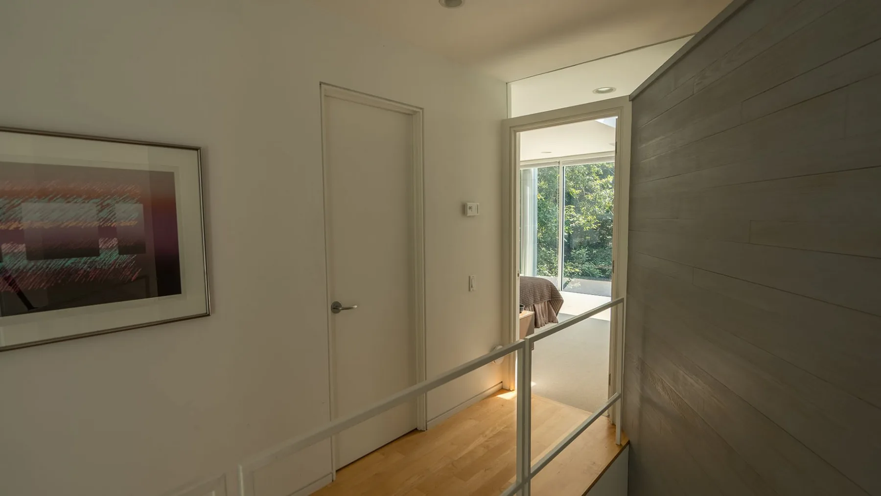 A bright interior hallway with a framed picture and a view into a sunlit room.