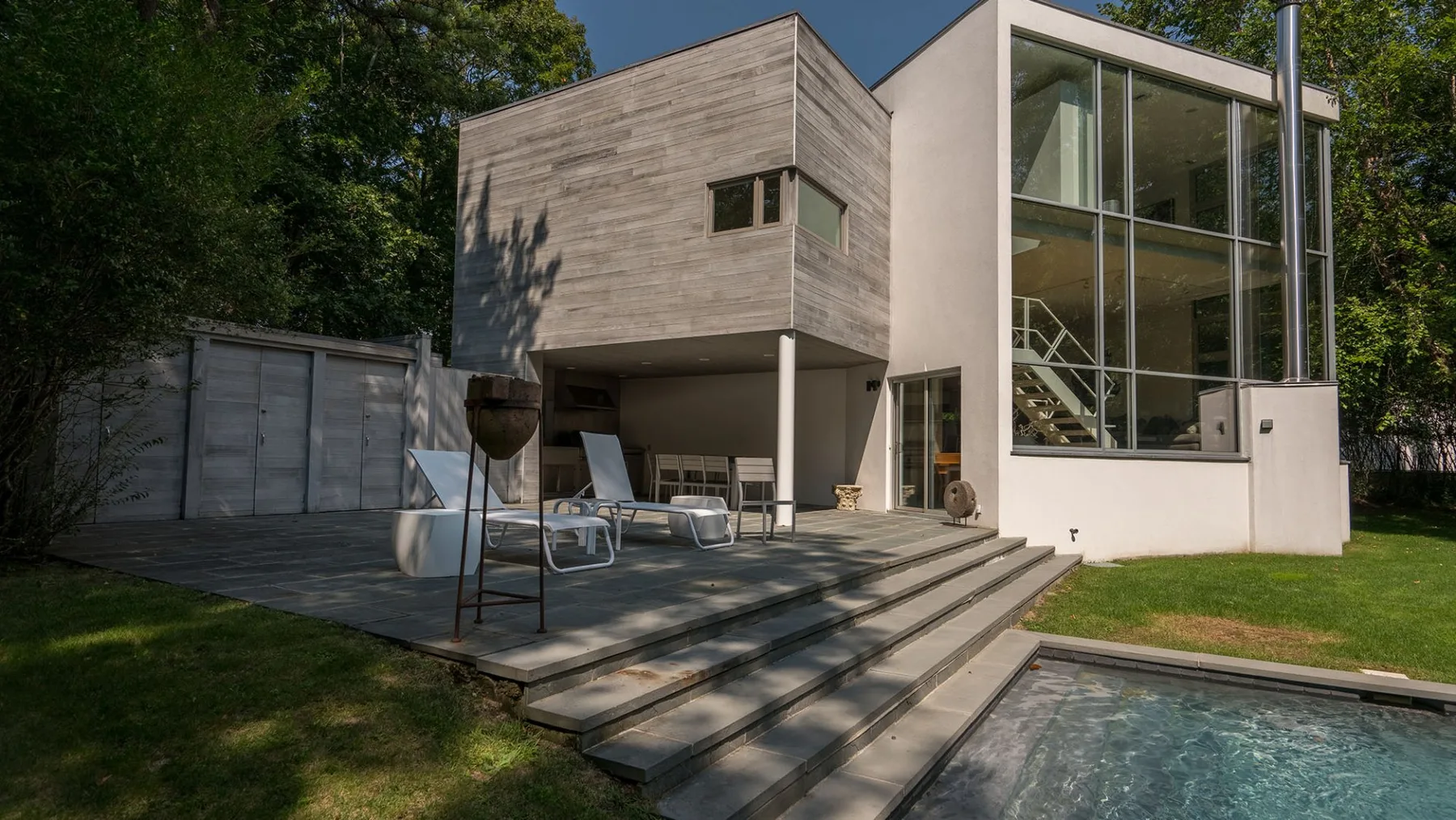 Una casa moderna con fachada acristalada da a un patio junto a una piscina.