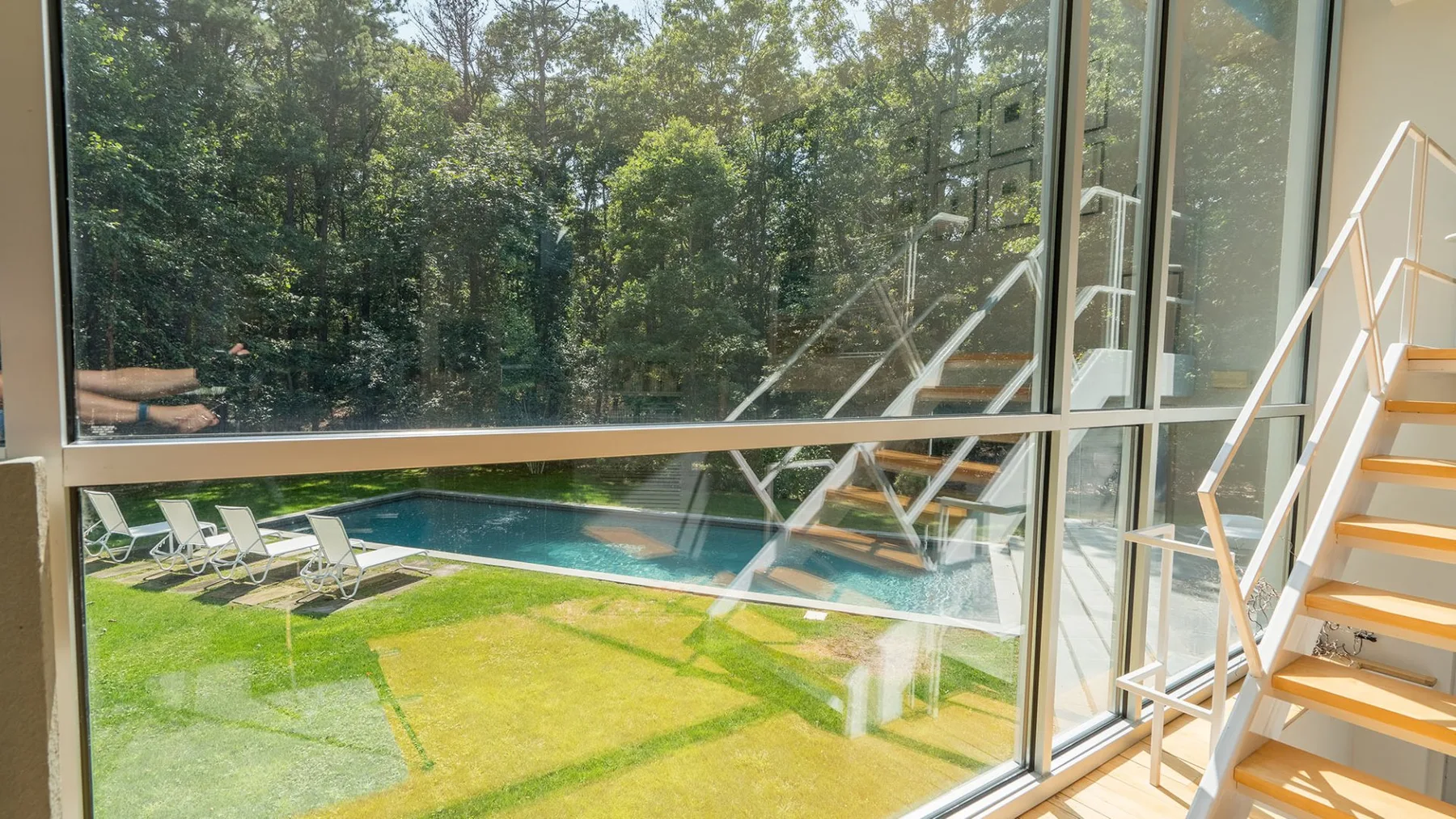 A glass-walled room overlooks a swimming pool and green lawn.