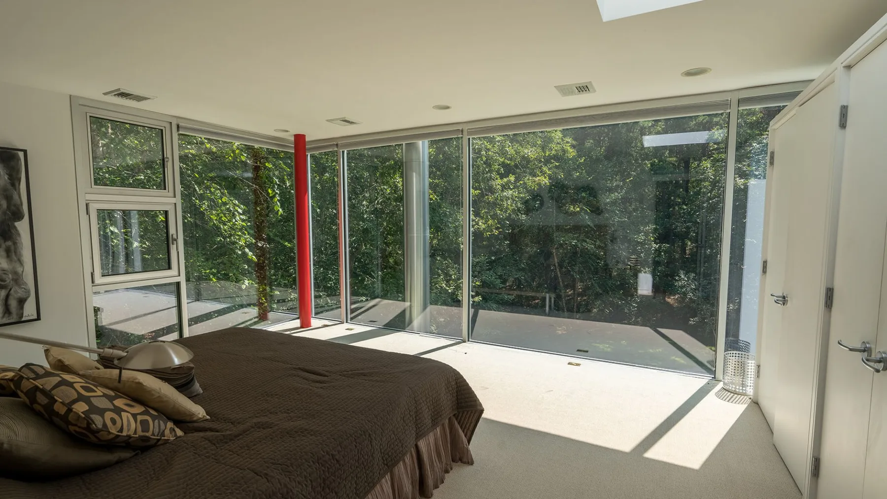 A bedroom with a bed beside large windows overlooking greenery.