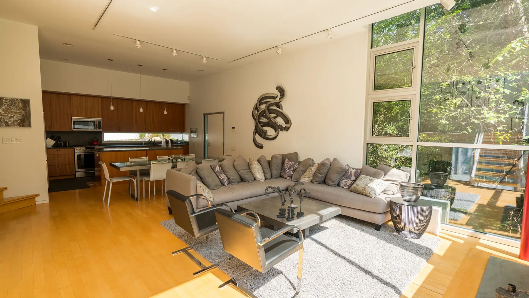 A bright living room with seating beside large windows and an open kitchen.