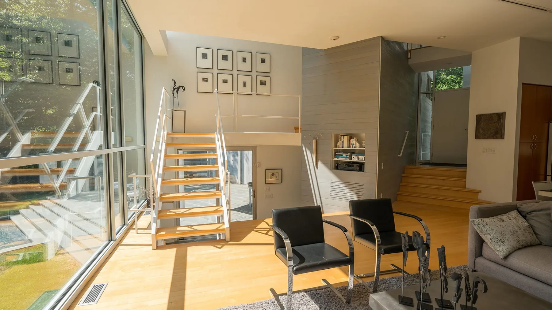 A bright living area with large windows, seating, and a staircase.