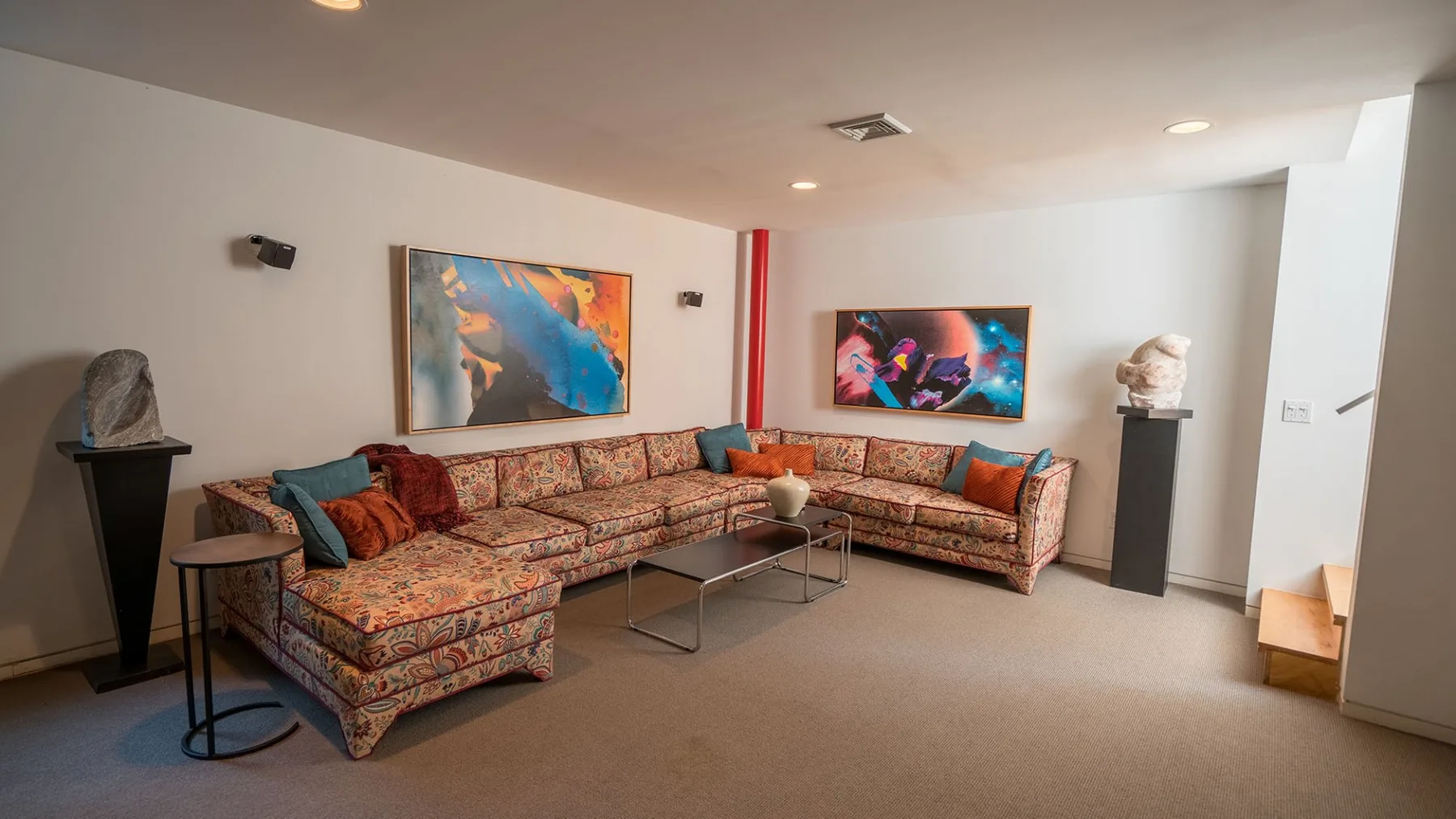 A living room with patterned seating, artwork, and a glass coffee table.