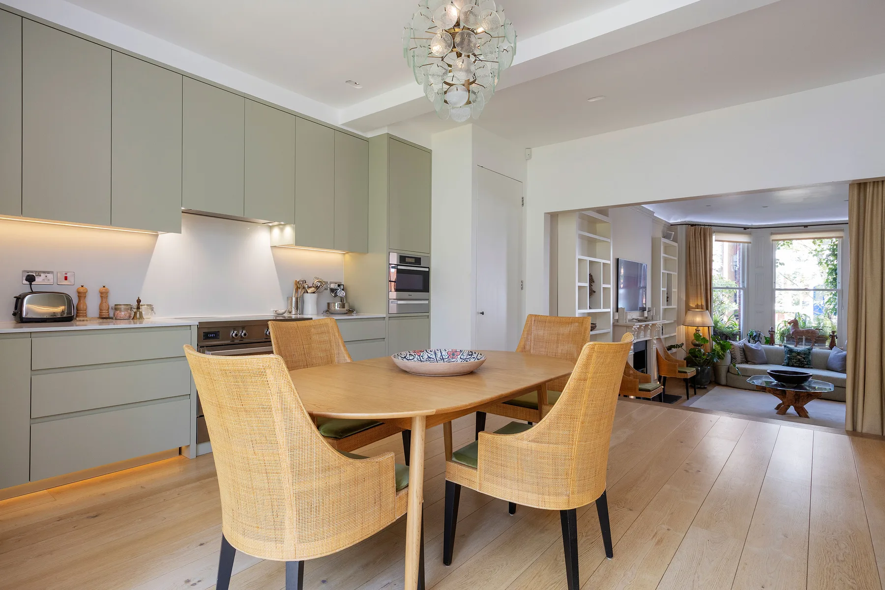 A dining area with a wooden table and woven seating beside an open kitchen.