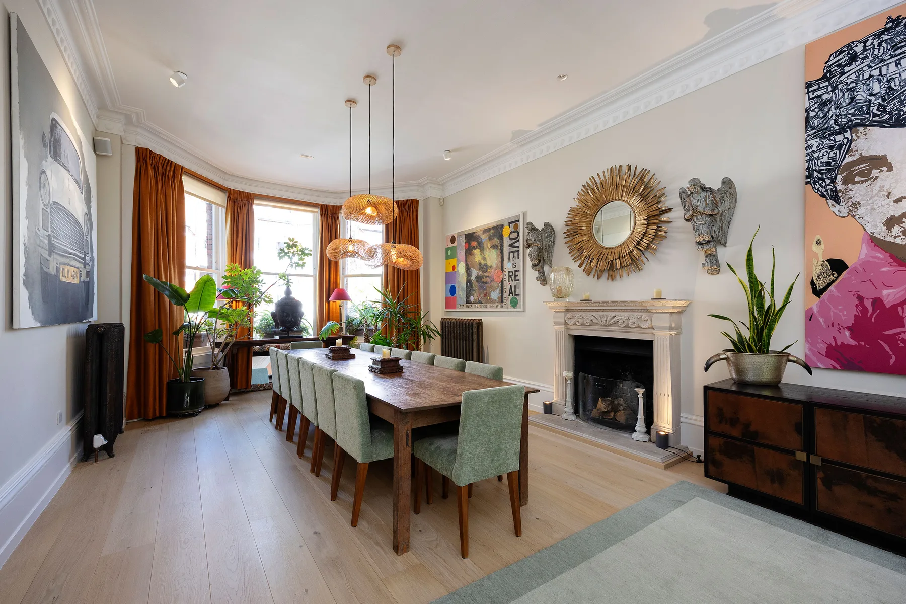 A bright dining room with a long wooden table, green seating, and a fireplace.