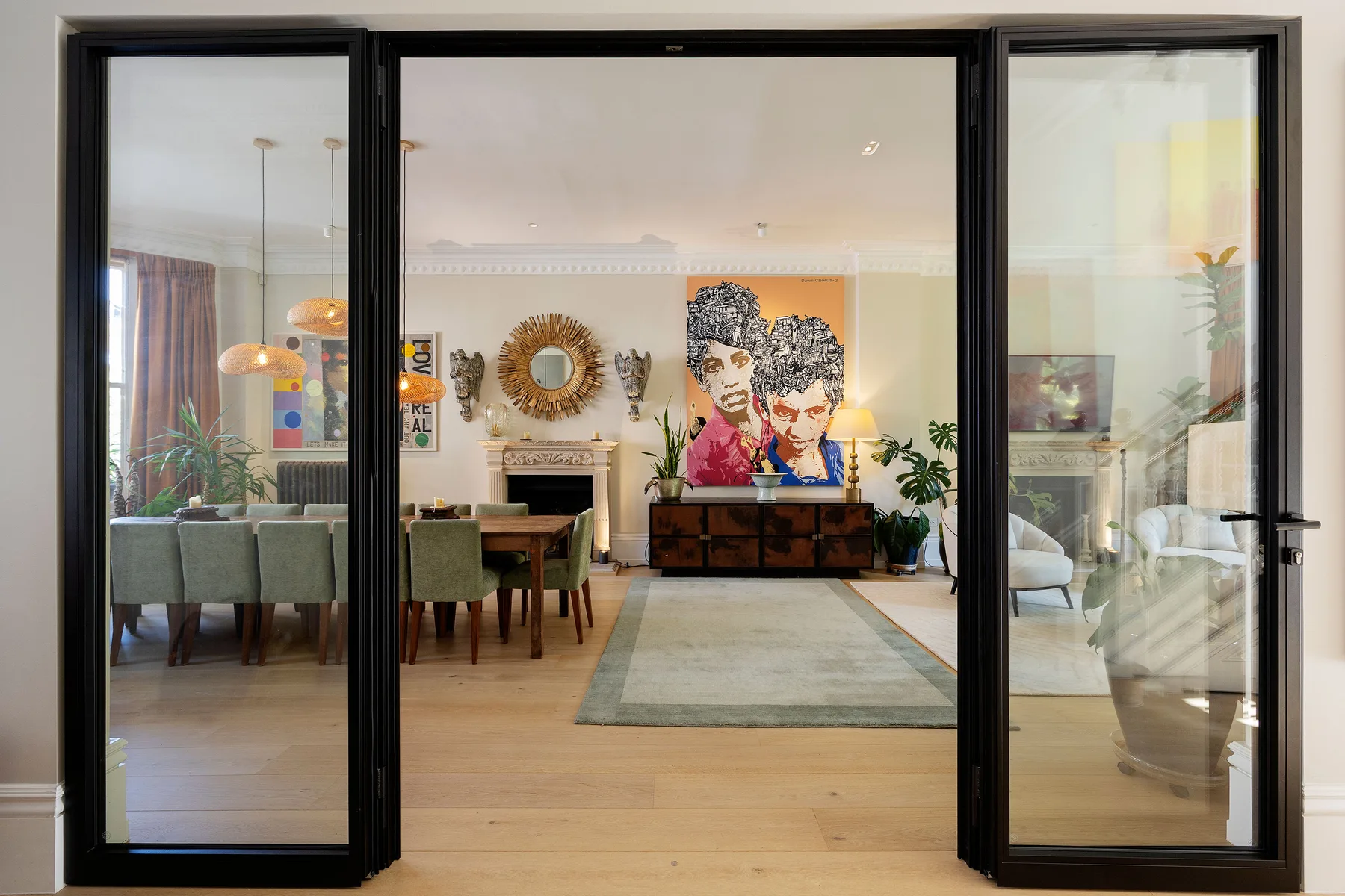 A bright living and dining room with a rug, seating, and colorful artwork.