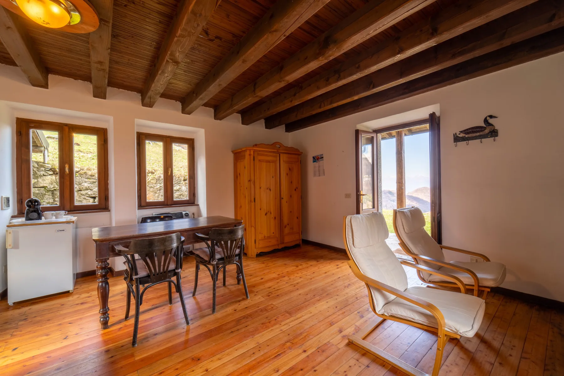 Una habitación con suelo de madera, mesa y asientos junto a una ventana luminosa.