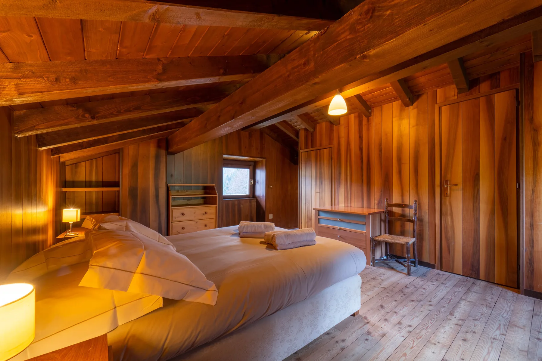 Un dormitorio cálidamente iluminado con una cama grande y paredes revestidas de madera.