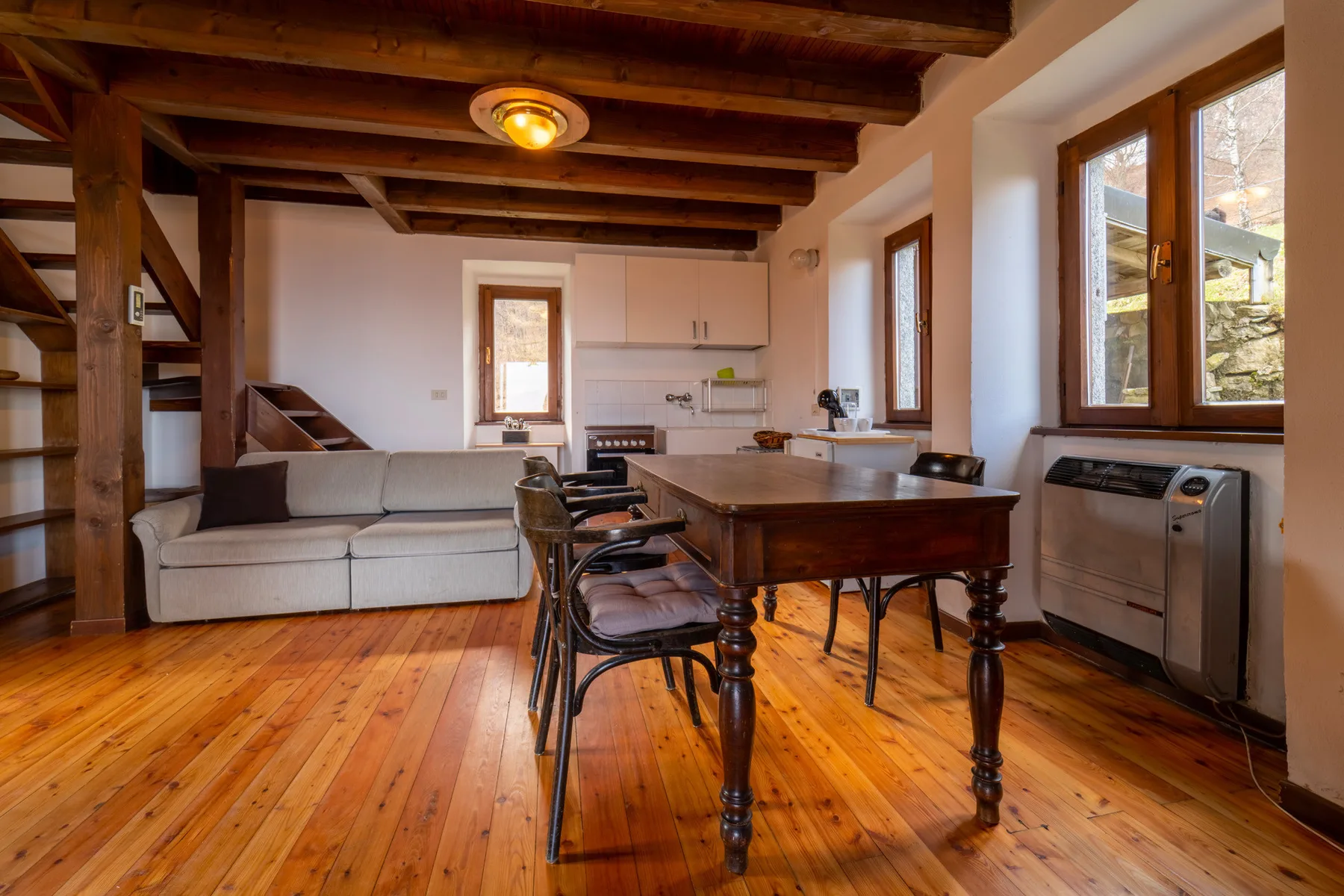 Una sala de estar y comedor con sofá, mesa de madera y cocina al fondo.