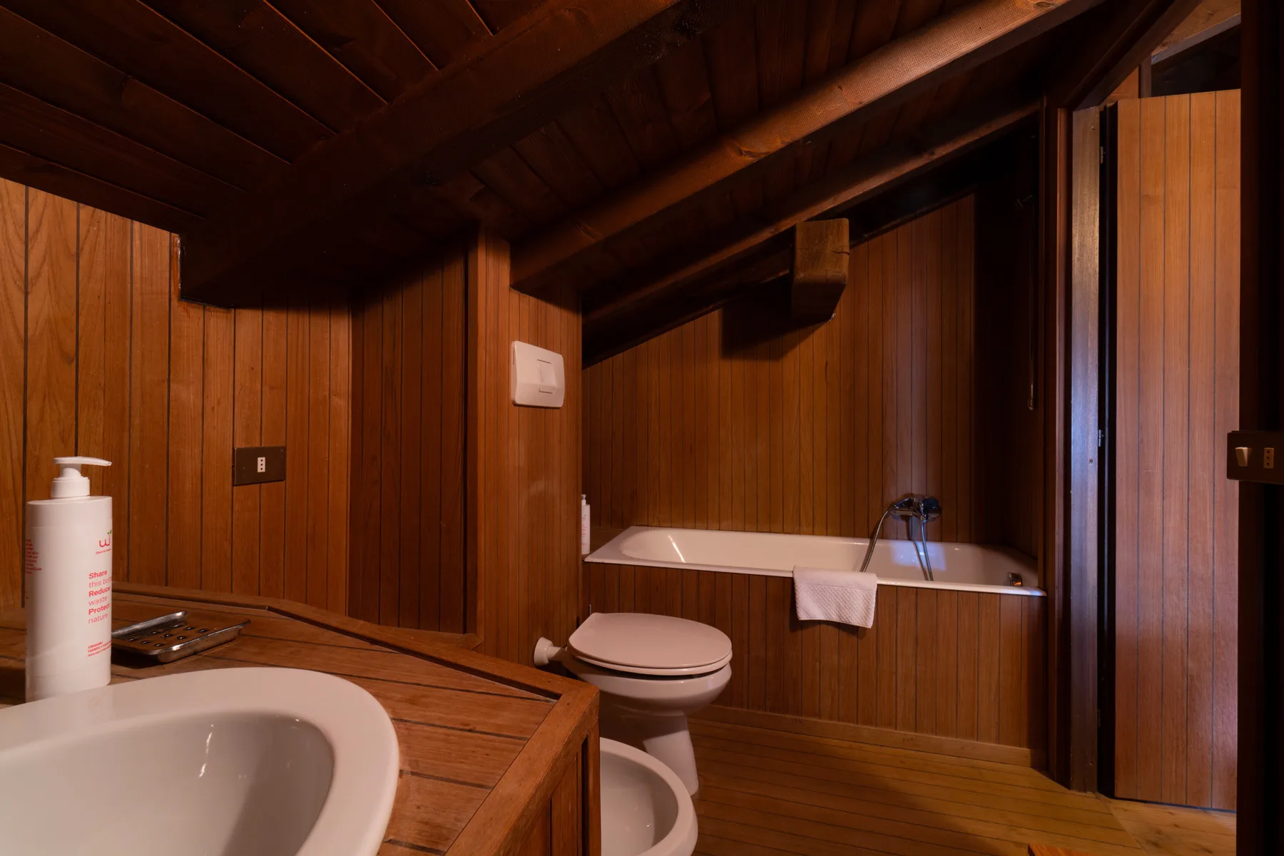 Un baño revestido de madera con bañera e inodoro.