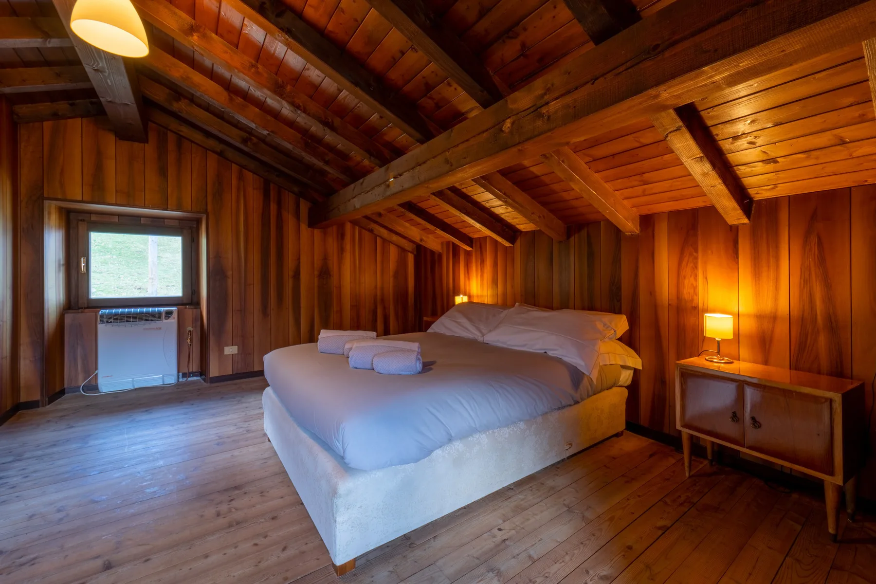 Un dormitorio con una cama grande bajo un techo de madera inclinado.
