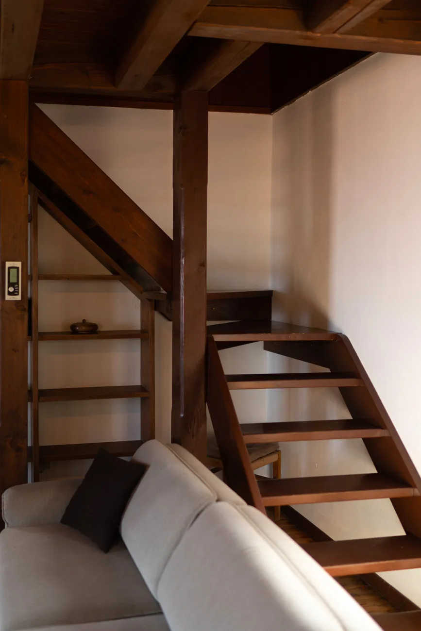 Una zona de estar con asientos claros bajo una escalera y vigas de madera.