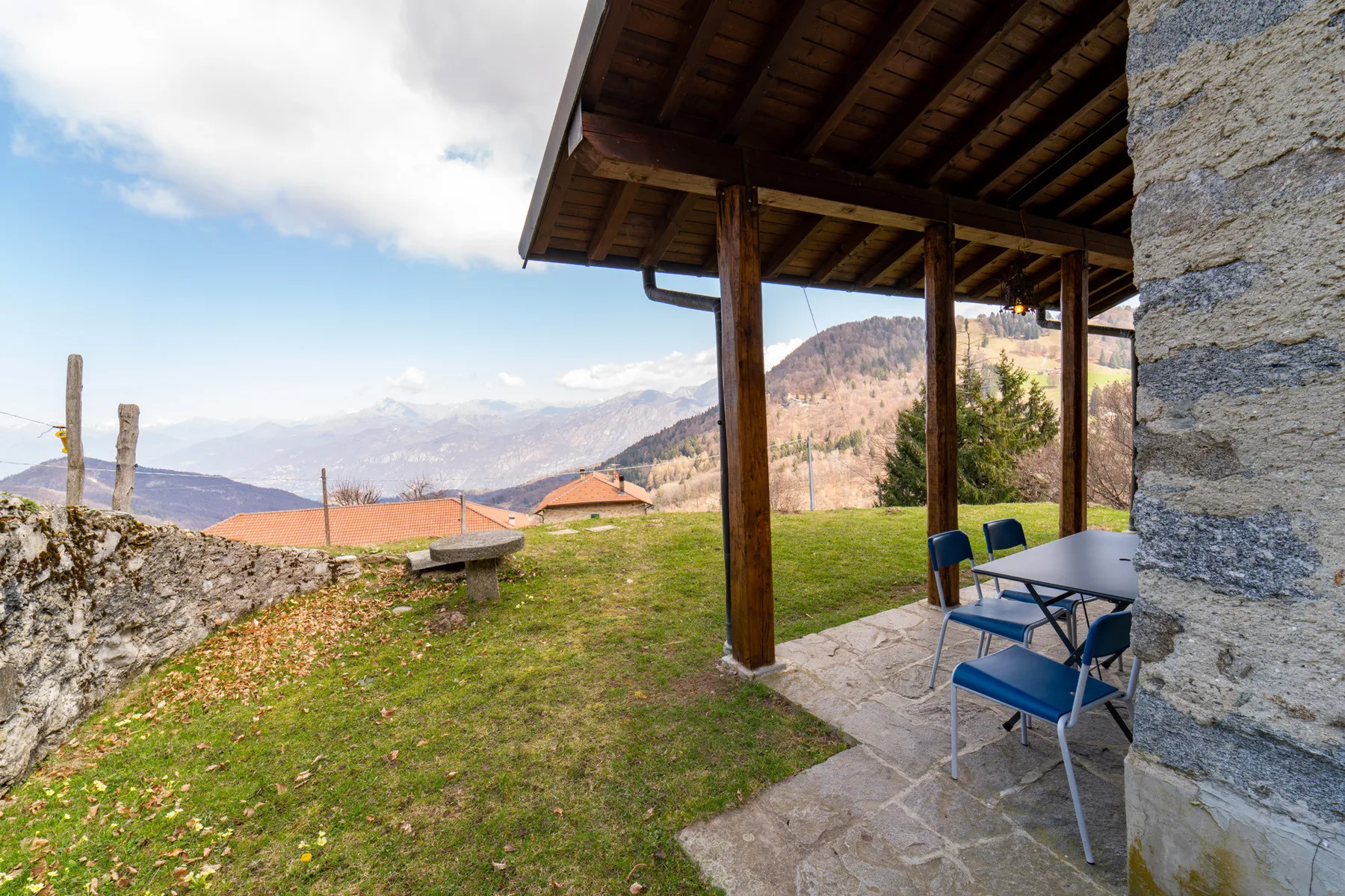 Un patio cubierto con una mesa y sillas ofrece vistas a un paisaje montañoso.