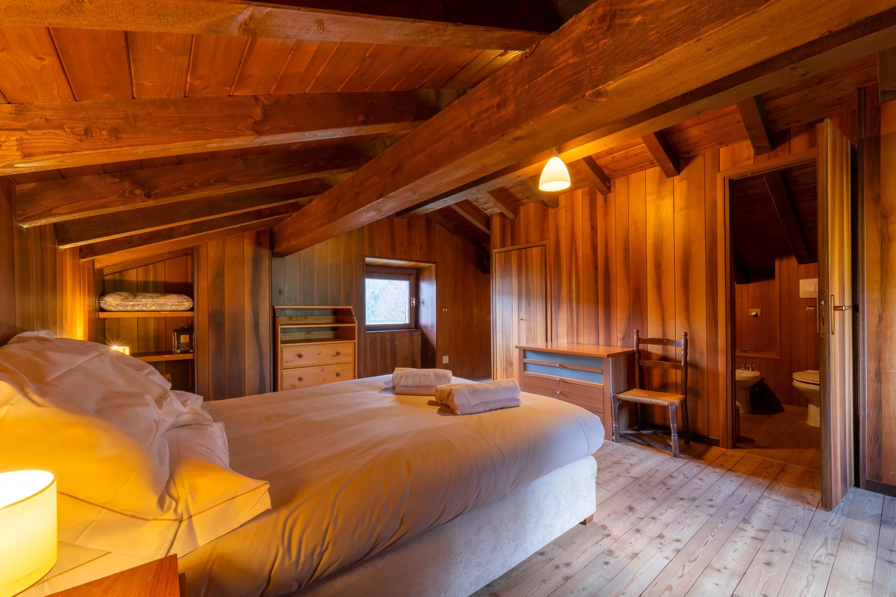 Un dormitorio revestido de madera con una cama, toallas dobladas y vigas expuestas en el techo.