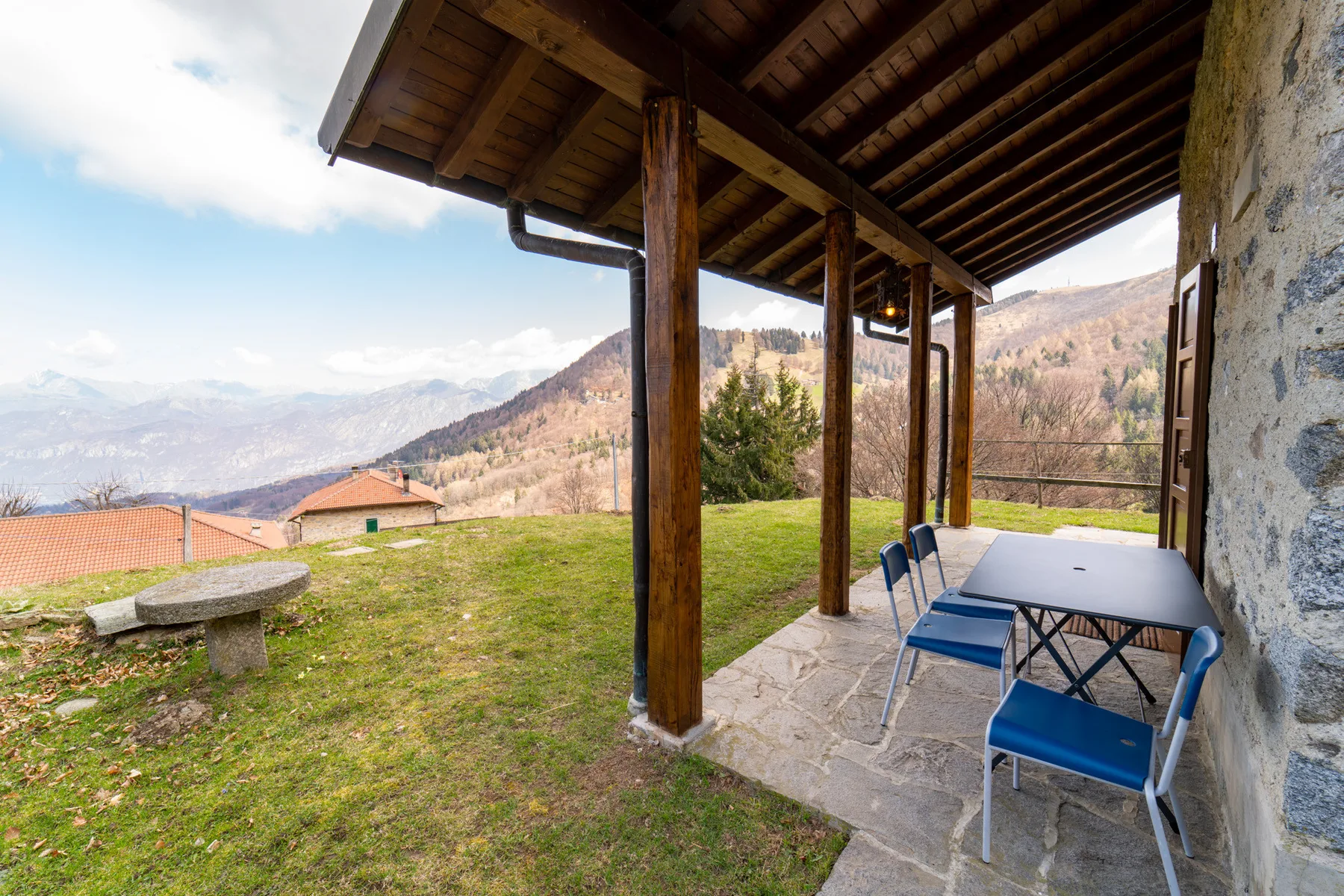 Un patio cubierto con mesa y sillas da a un jardín con césped y colinas lejanas.