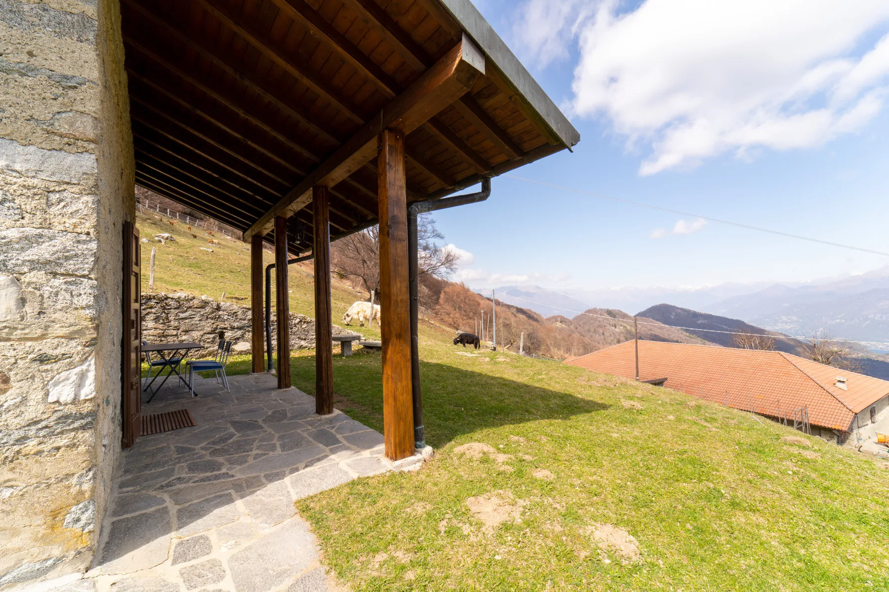 Un patio de piedra cubierto da a una ladera cubierta de hierba con vistas a las montañas.