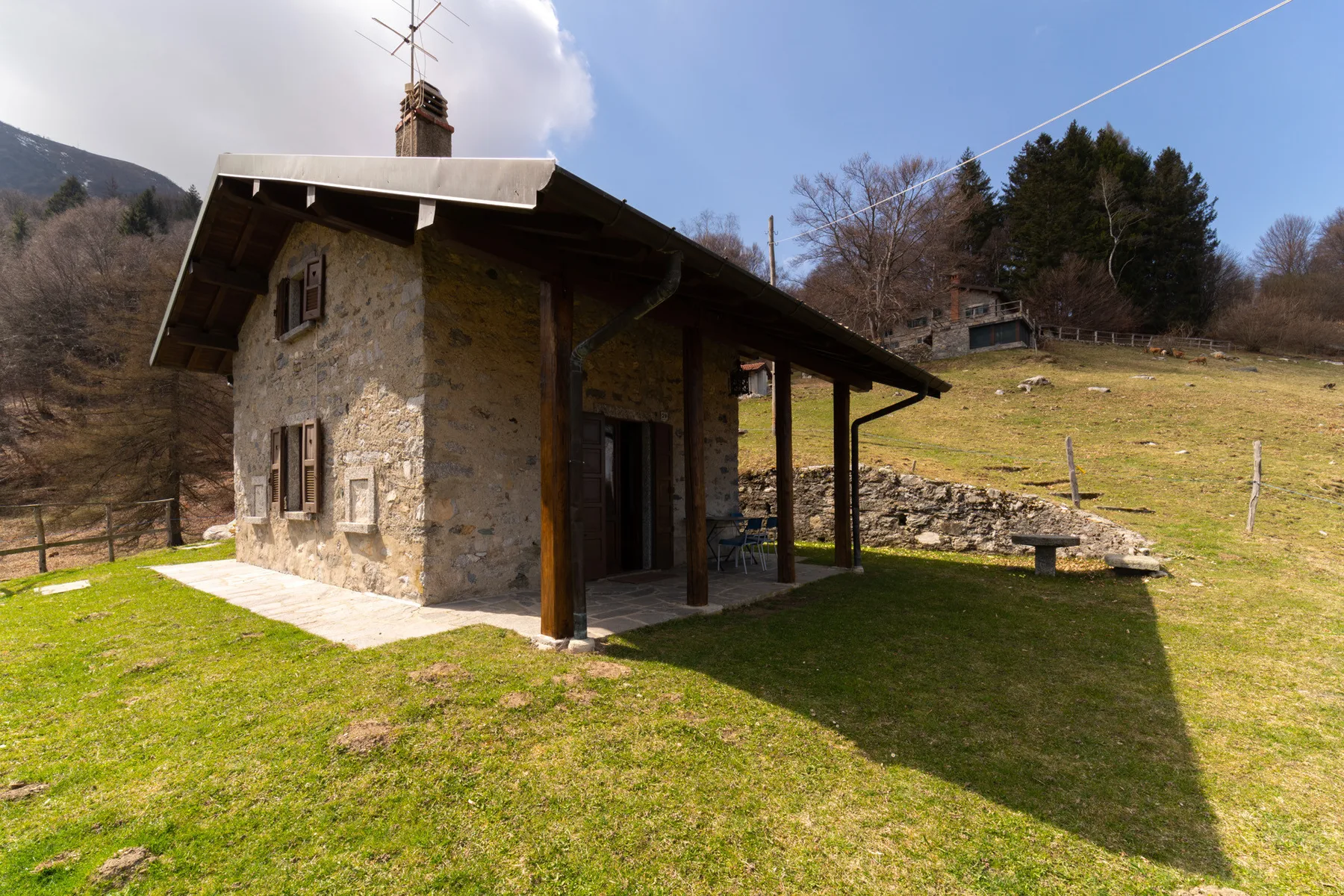 Una pequeña casa de piedra está junto a una ladera cubierta de hierba.
