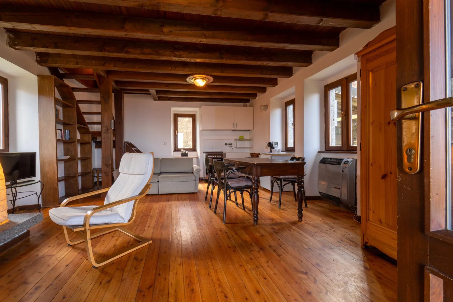 Sala de estar y comedor con suelo de madera, vigas a la vista y una mesa.