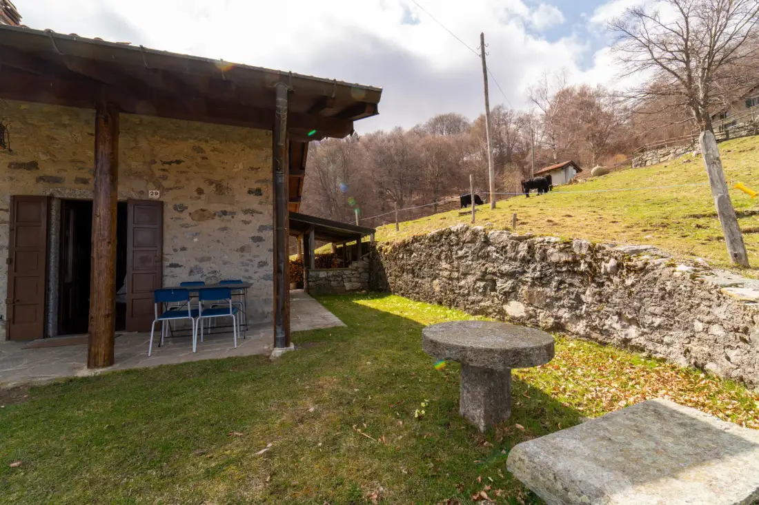 Un edificio de piedra da a una zona de estar al aire libre con césped, junto a un muro bajo de piedra.