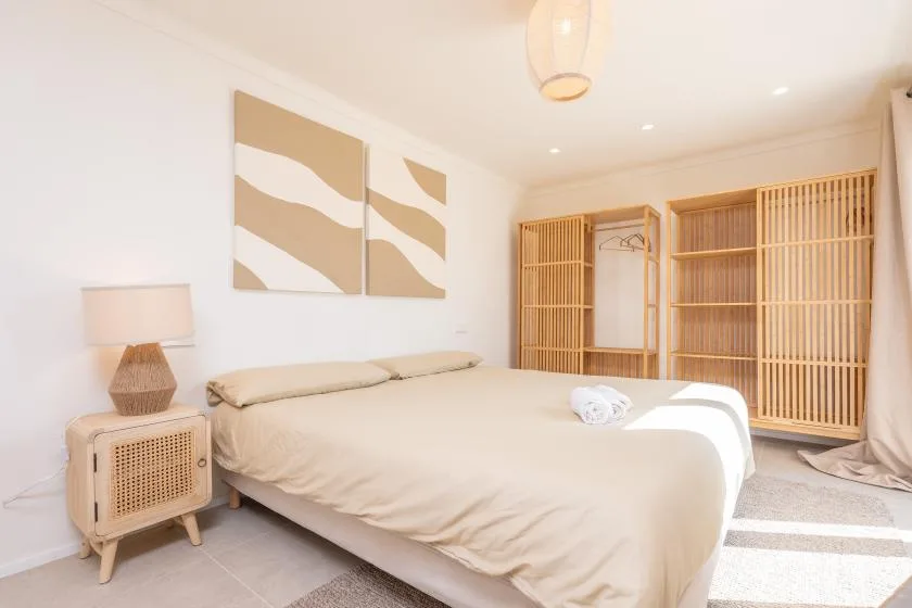 Un dormitorio luminoso con una cama, cuadros y un armario de listones.