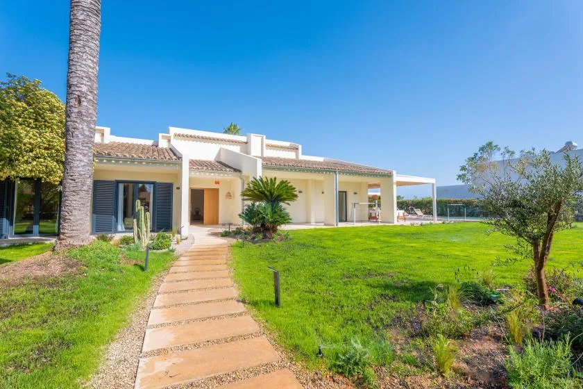Una casa de una planta se abre a un amplio césped verde bajo un cielo azul despejado.