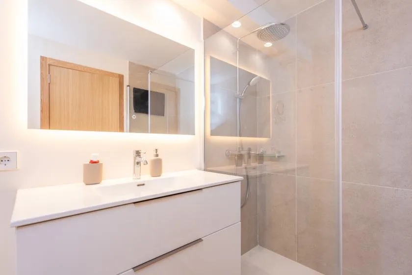 Un baño luminoso con un mueble blanco y una ducha con mampara de vidrio.