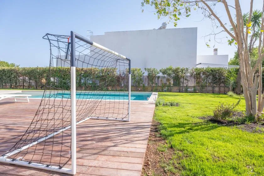 Una zona deportiva en el patio con una portería junto a una piscina y césped.