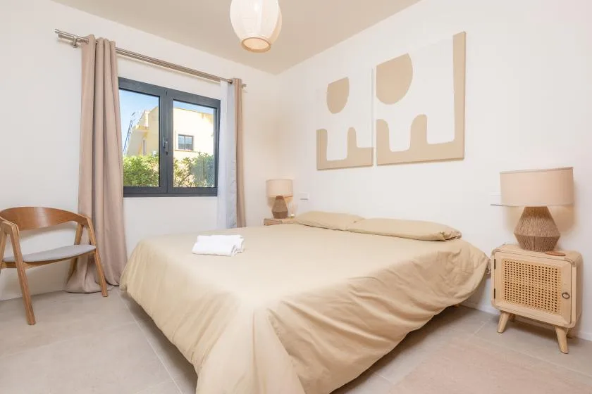 Un dormitorio con una cama, una ventana y decoración en tonos neutros.