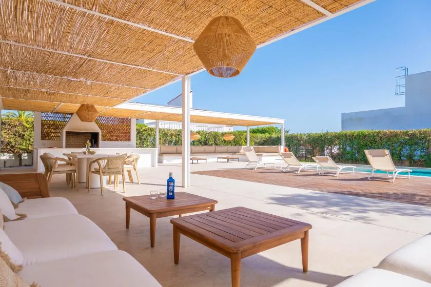Una zona de descanso al aire libre con asientos acolchados y mesas de madera junto a una piscina.