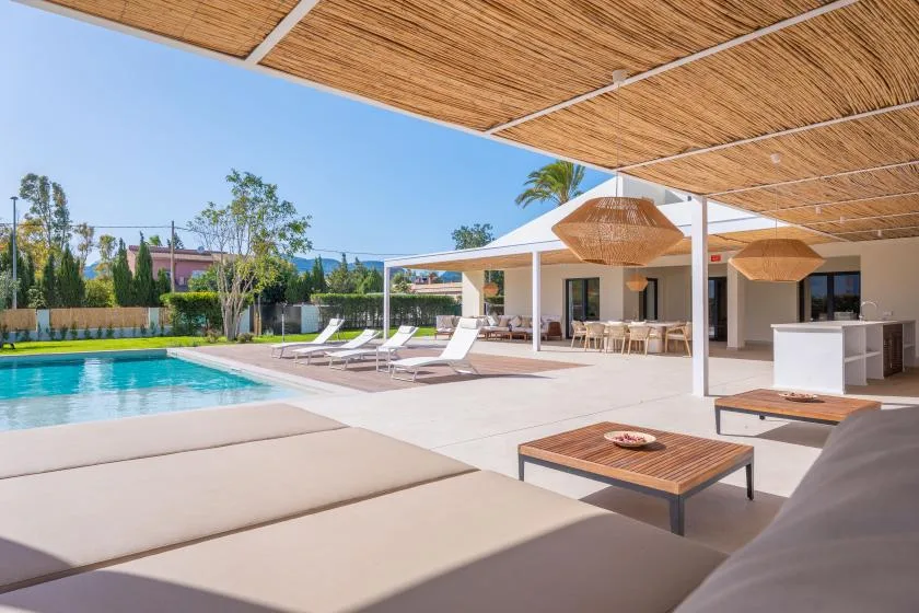 Un patio junto a la piscina con asientos a la sombra y una zona de comedor al aire libre.