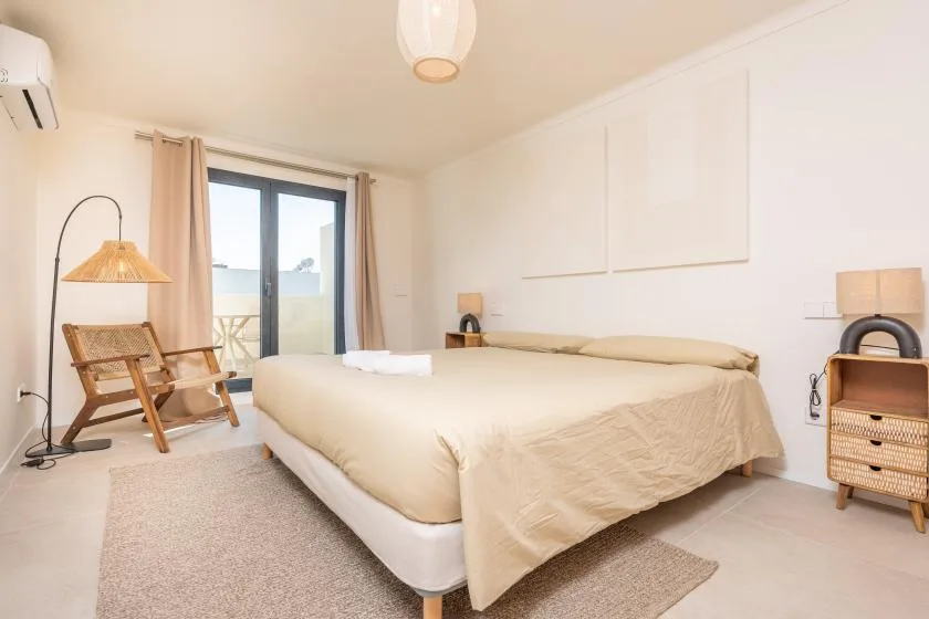 Un dormitorio luminoso con una cama, una ventana y una silla tejida.