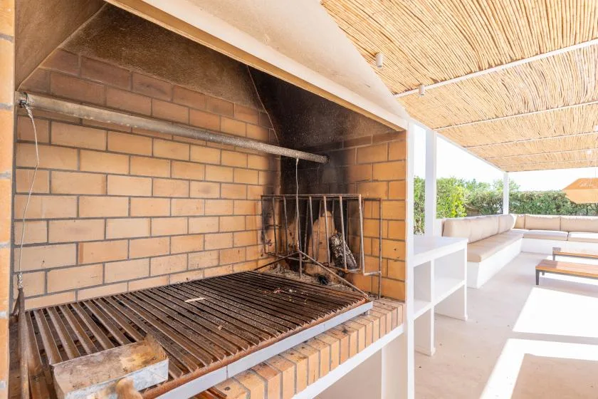 Una parrilla de ladrillo está junto a una zona de estar al aire libre bajo un toldo.