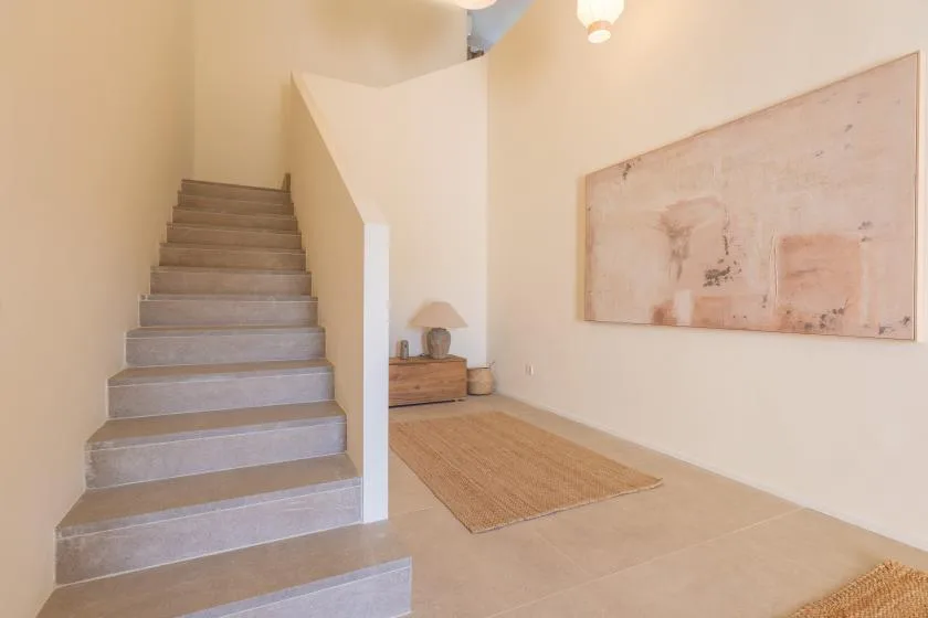 Un pasillo interior luminoso con una escalera, una alfombra tejida y arte en la pared.