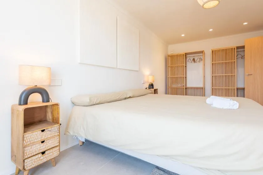 Un dormitorio luminoso con una cama grande y armarios de madera abiertos.