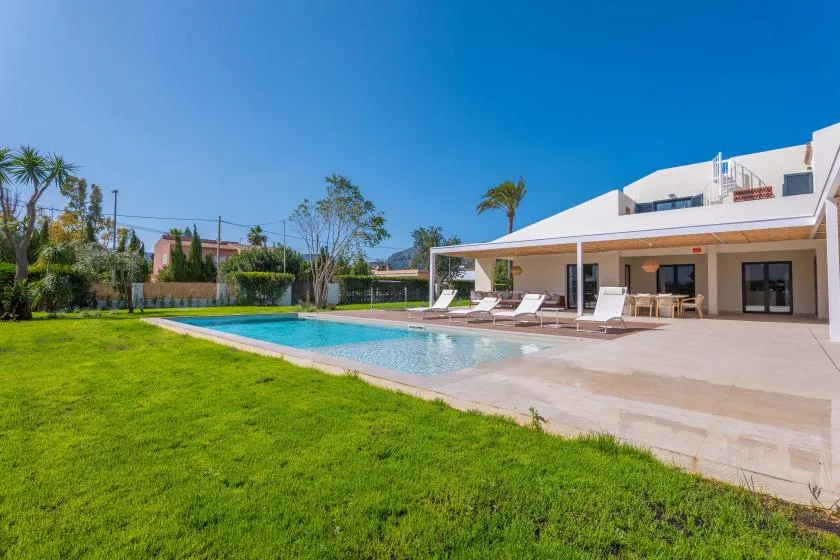 Una piscina y un césped junto a una casa blanca moderna.