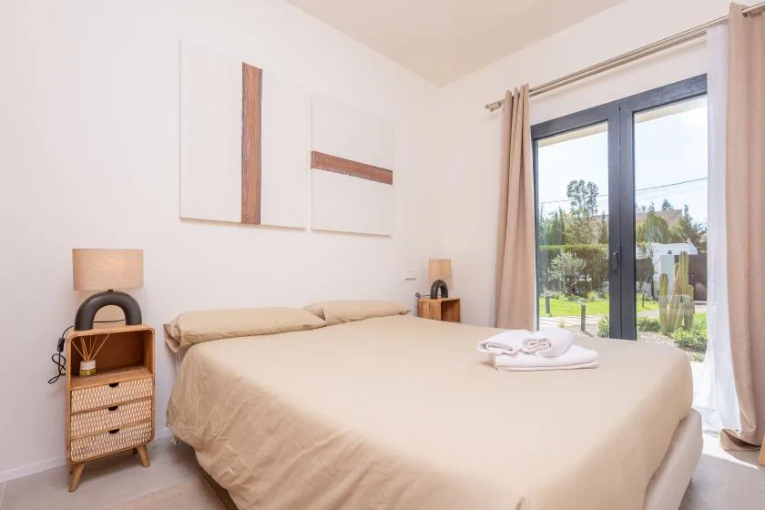 Un dormitorio luminoso con una cama grande y puertas de vidrio que dan a un jardín.