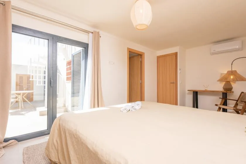 Un dormitorio luminoso con una cama grande y puertas correderas de cristal que dan a un patio.