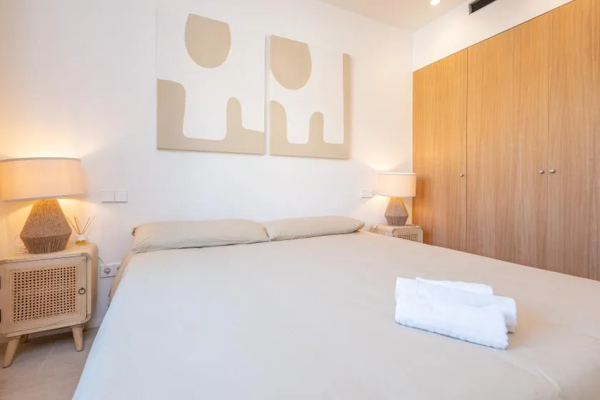 Un dormitorio luminoso con una cama bien tendida y un armario de madera.