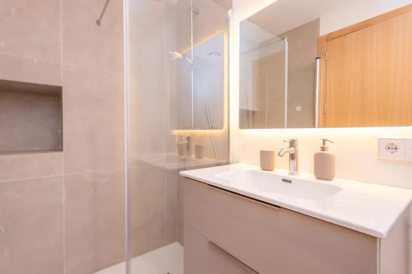 Un baño luminoso con una ducha de vidrio y un lavabo con mueble largo.
